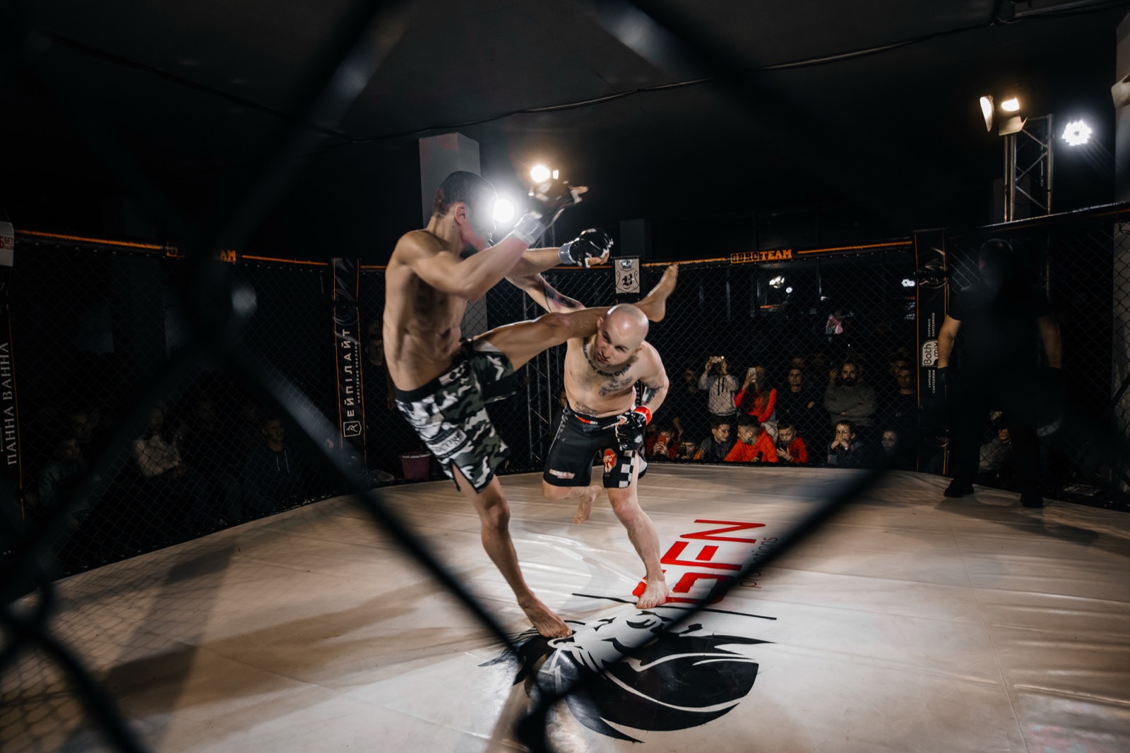 A fighter lands a high kick during a bout watched by the arena audience.