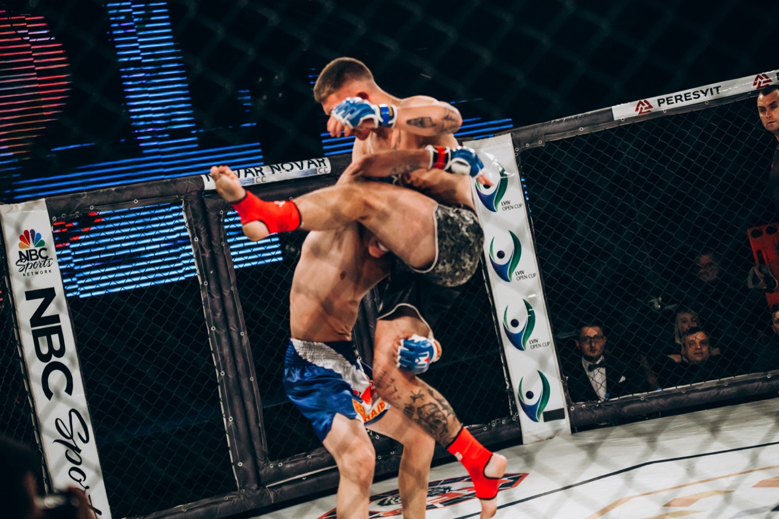 A fighter lifts an opponent while attempting a takedown against the cage.