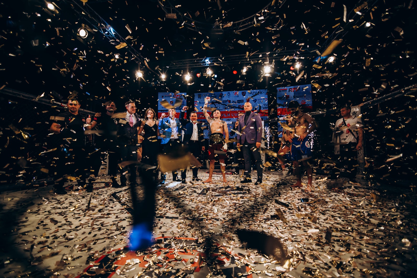 Fighters and officials during the closing ceremony in a cage filled with gold confetti.